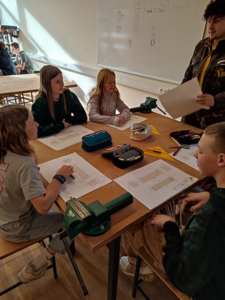 Bei der TischlerTrophy sitzen Kinder an einem Tisch und besprechen das Projekt